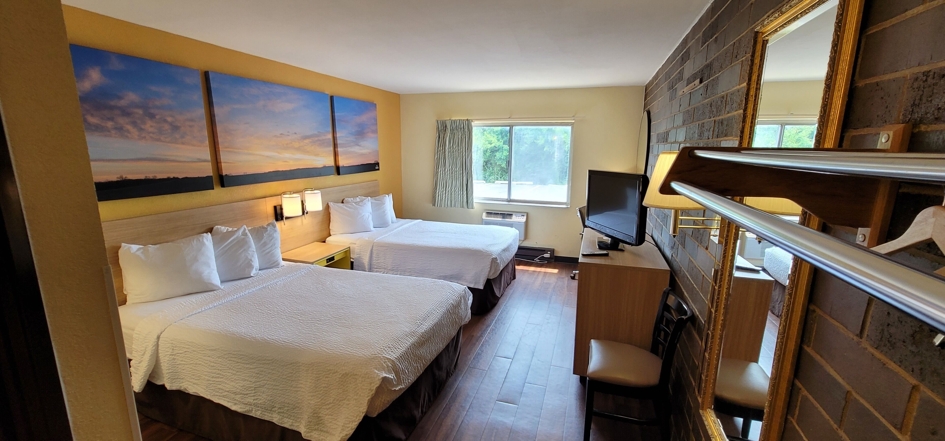 A hotel room with two beds, a desk, a TV, and a large mirror.