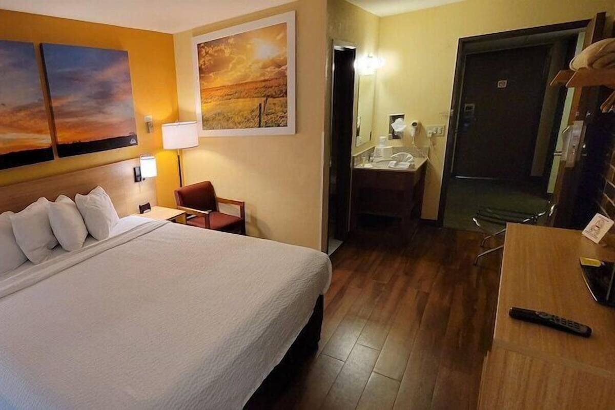 A hotel room with a bed, nightstand, lamp, and wall art.