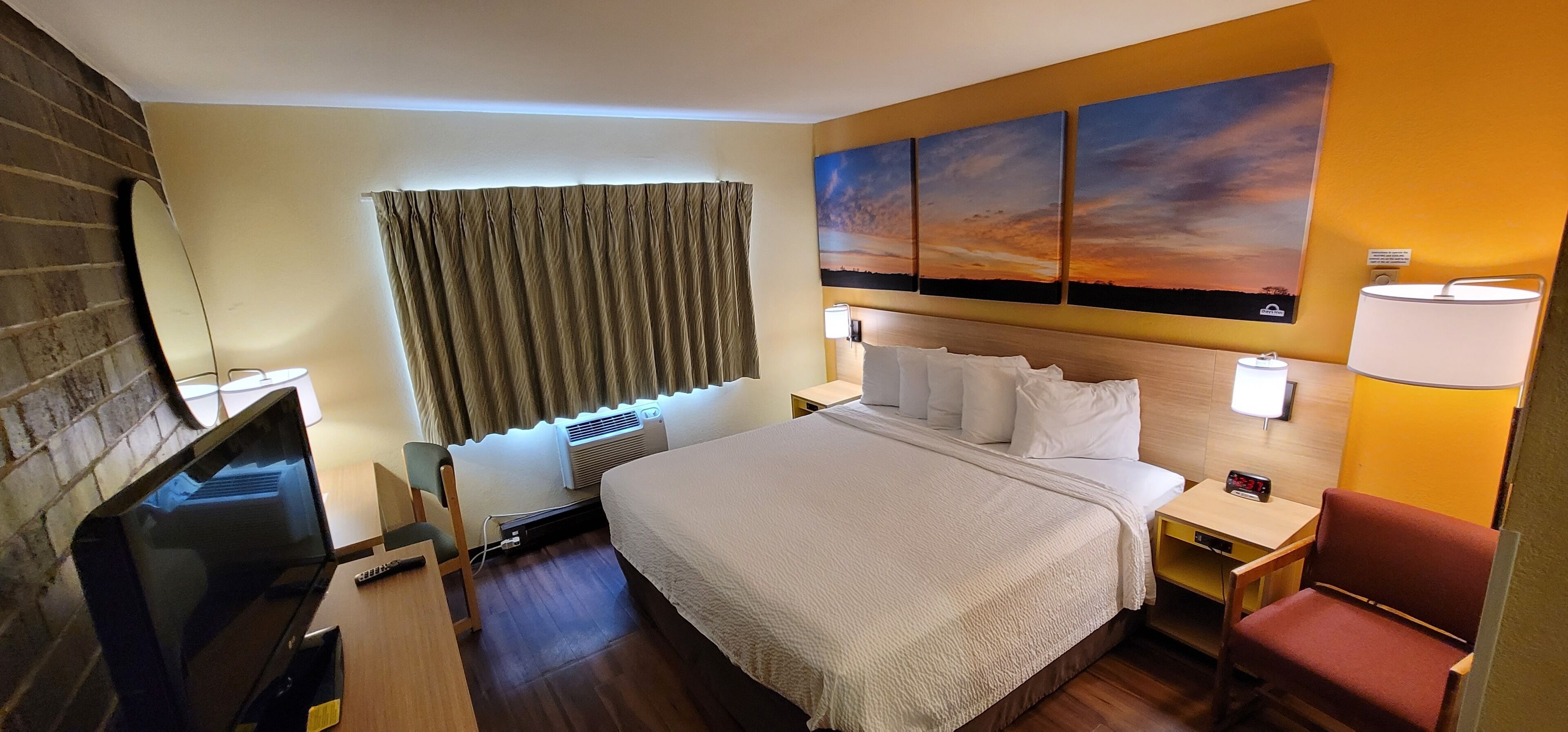 Una habitación de hotel con cama, televisión, escritorio, silla y un cuadro en la pared.