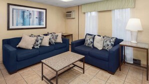 A hotel room with two blue sofas, a small table, a framed abstract painting, an air conditioning unit, and a lamp. - Days Inn by Wyndham Rockford I-90 Casino District (Rockford)