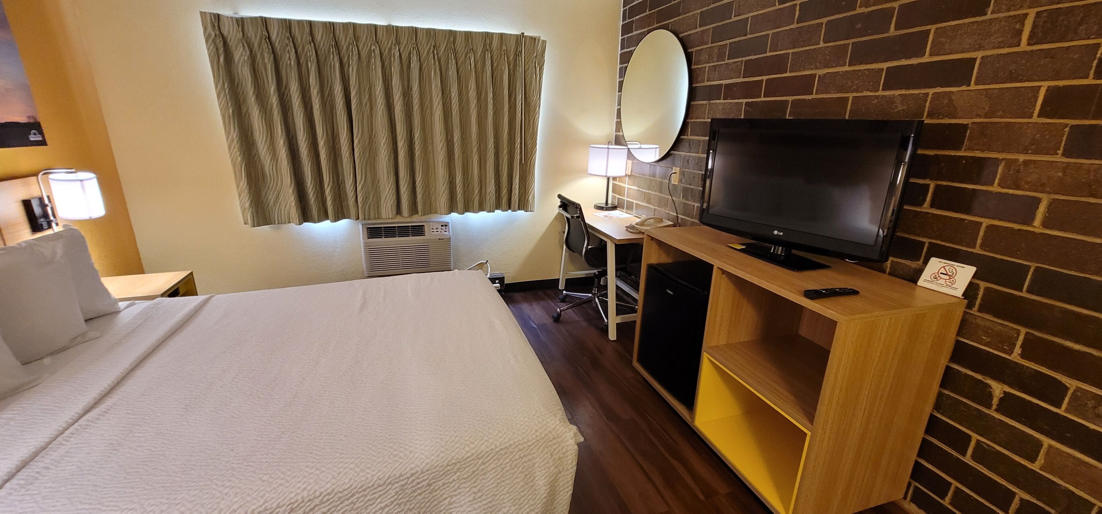 Ett hotellrum med en säng, ett skrivbord med en tv, en lampa och en spegel på väggen.