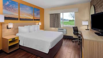 Habitación de hotel con una cama grande, un escritorio con televisor, una ventana con cortinas y una obra de arte en la pared.