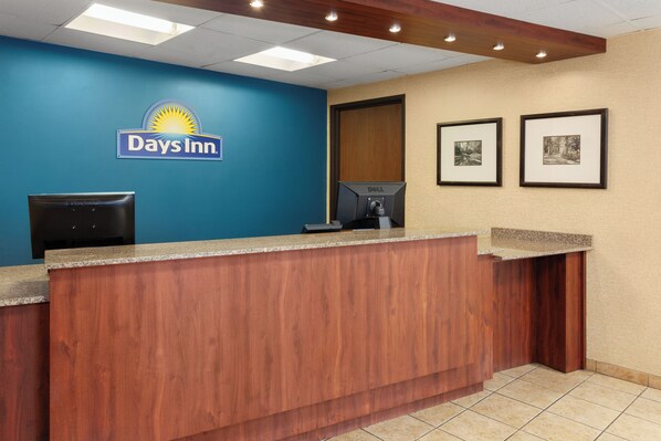 Una recepción con el letrero de Days Inn, una computadora, cuadros en la pared y un mostrador de madera.