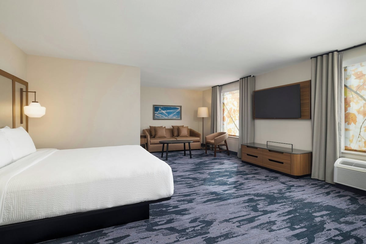 A hotel room with a large bed, a sofa, a small table, and a TV mounted on the wall.