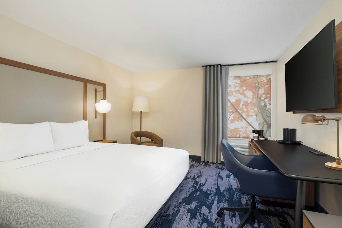 A hotel room with a large bed, a desk, a chair, a TV, and a window with curtains.