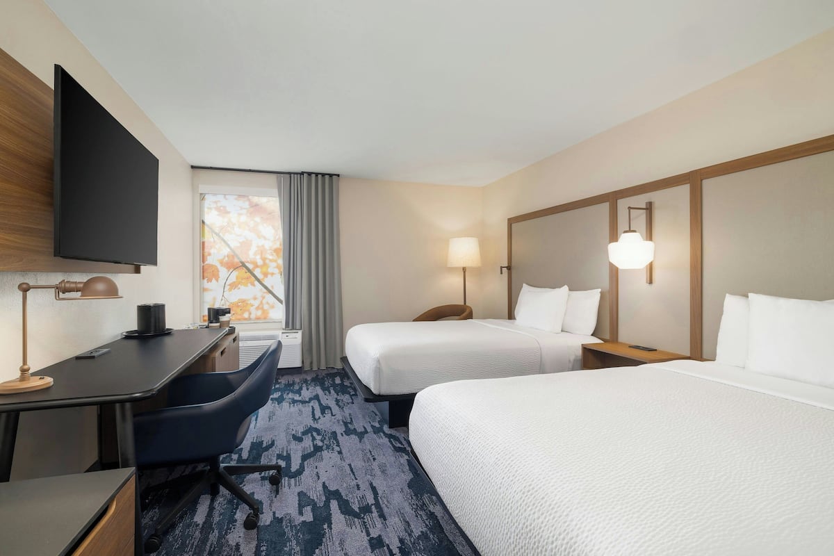 A hotel room with two beds, a desk, a chair, a TV, and a window with curtains.