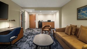 A hotel room with a desk, chair, sofa, and a kitchenette in the background. - Fairfield by Marriott Inn & Suites Clinton (Clinton)
