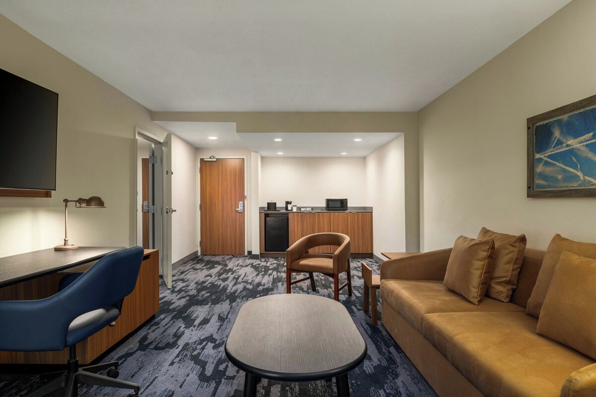 Ein Hotelzimmer mit Schreibtisch, Stuhl, Sofa und einer kleinen Küche im Hintergrund.