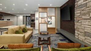 A modern hotel lobby with a sofa, coffee table, and a stone accent wall with a flat-screen TV. - Fairfield by Marriott Inn & Suites Clinton (Clinton)