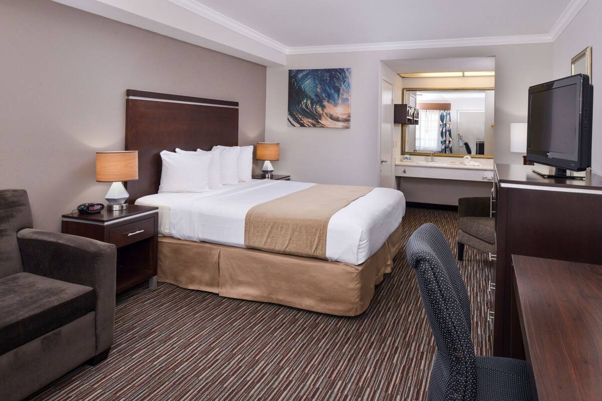 Une chambre d’hôtel comprenant un lit, des tables de chevet, un bureau, une chaise, une télévision, un miroir et un tableau au mur.