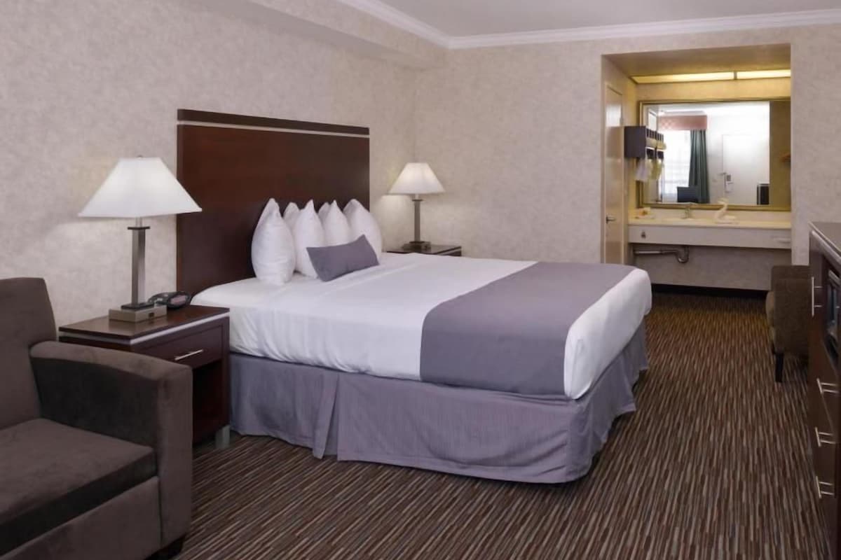 A hotel room with a bed, bedside tables, a chair, a desk, and a mirror.