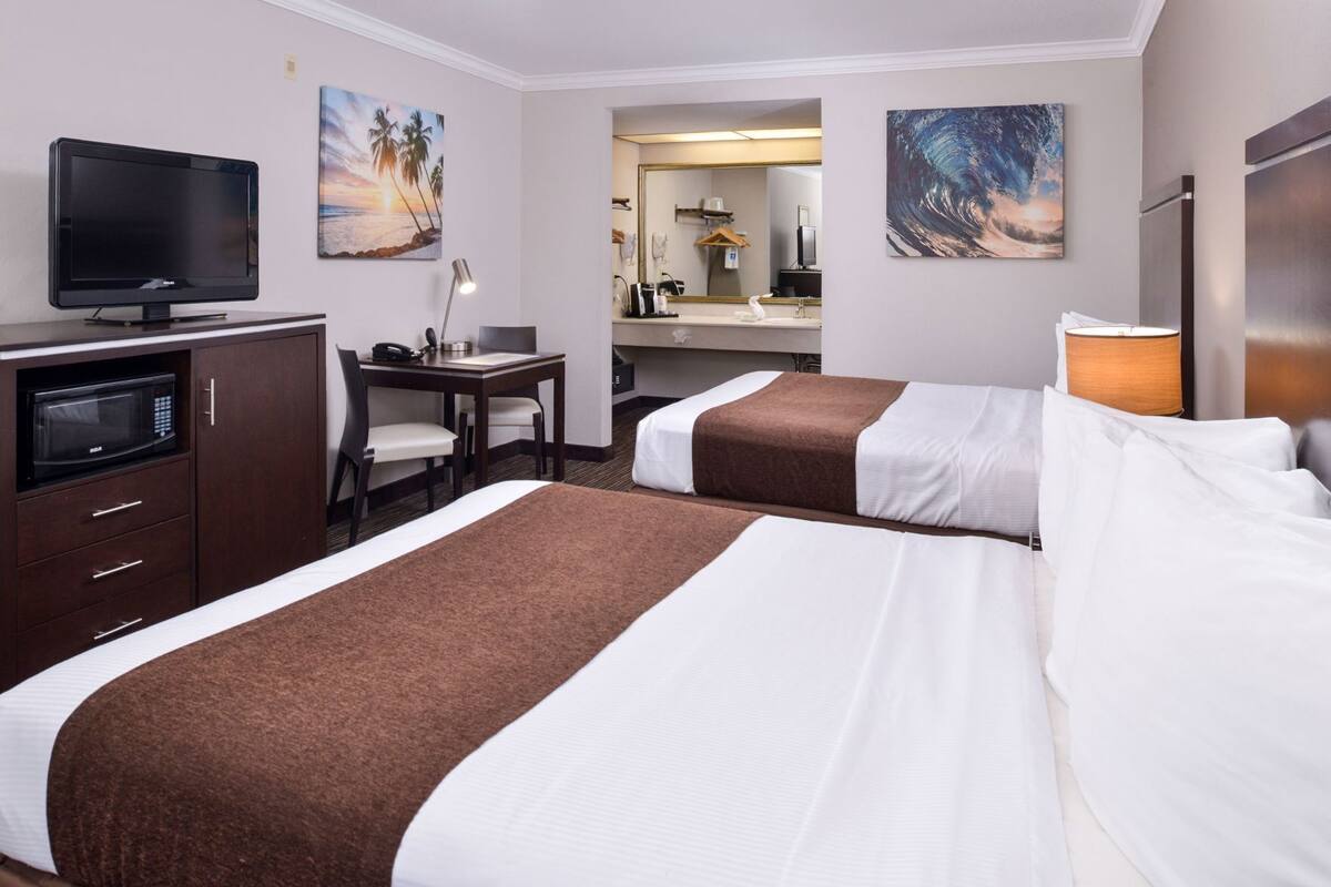Une chambre d’hôtel avec deux lits, un bureau, une télévision, un four à micro-ondes et des œuvres d’art accrochées aux murs.