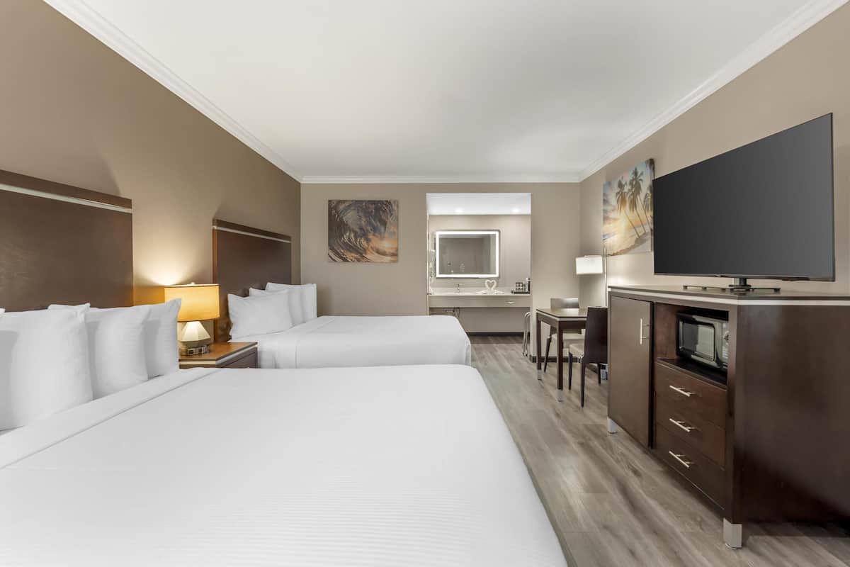 Une chambre d’hôtel avec deux lits, un bureau, une télévision, un miroir et des œuvres d’art accrochées aux murs.