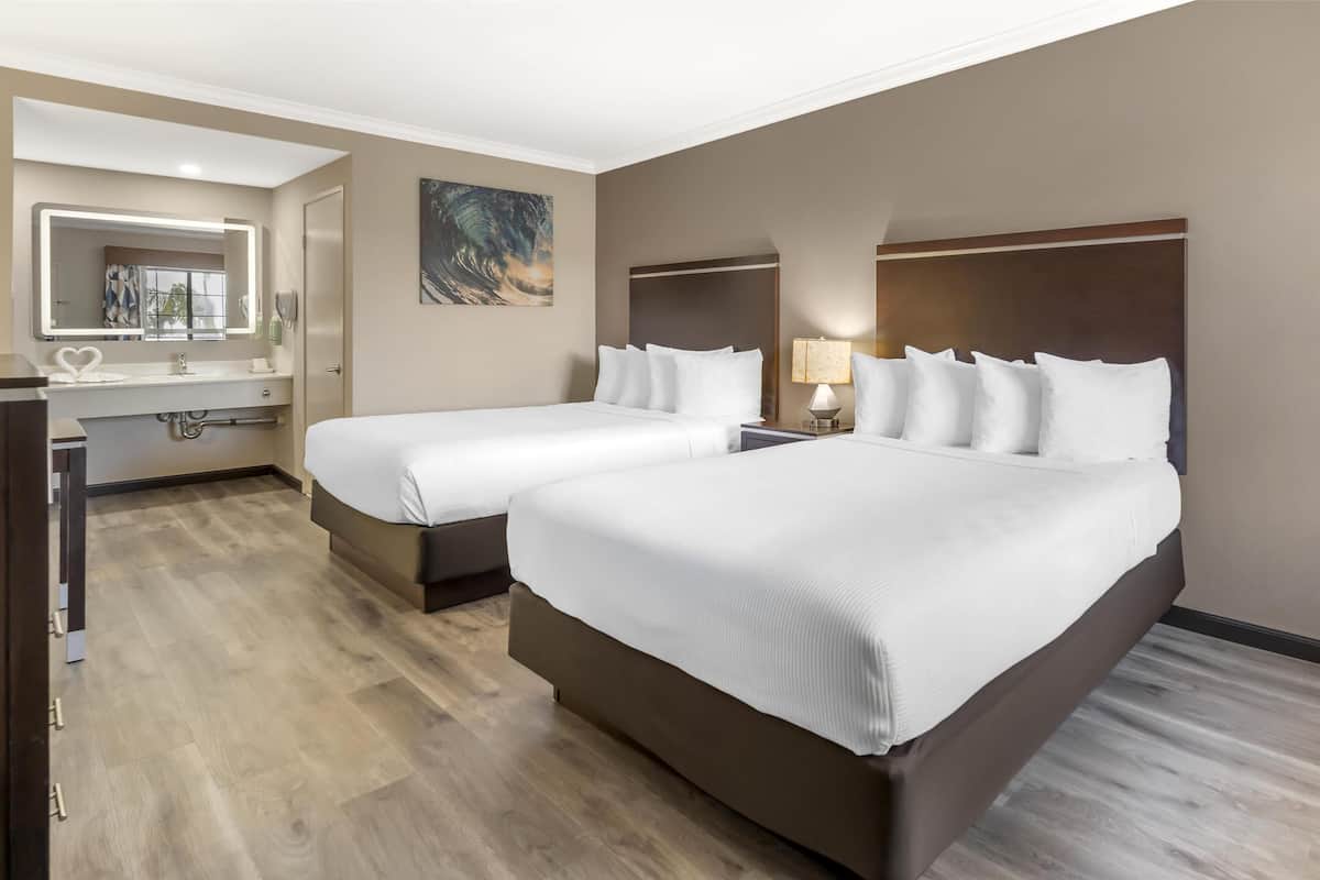 Une chambre d’hôtel avec deux lits, une salle de bain avec un miroir et un tableau au mur.