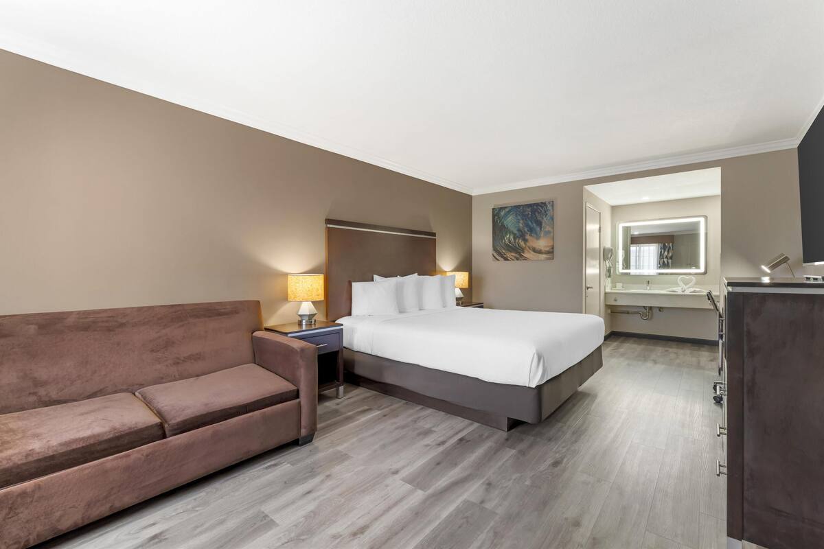 Une chambre d’hôtel avec un lit, un canapé, une table de chevet, une lampe, un miroir et un tableau au mur.