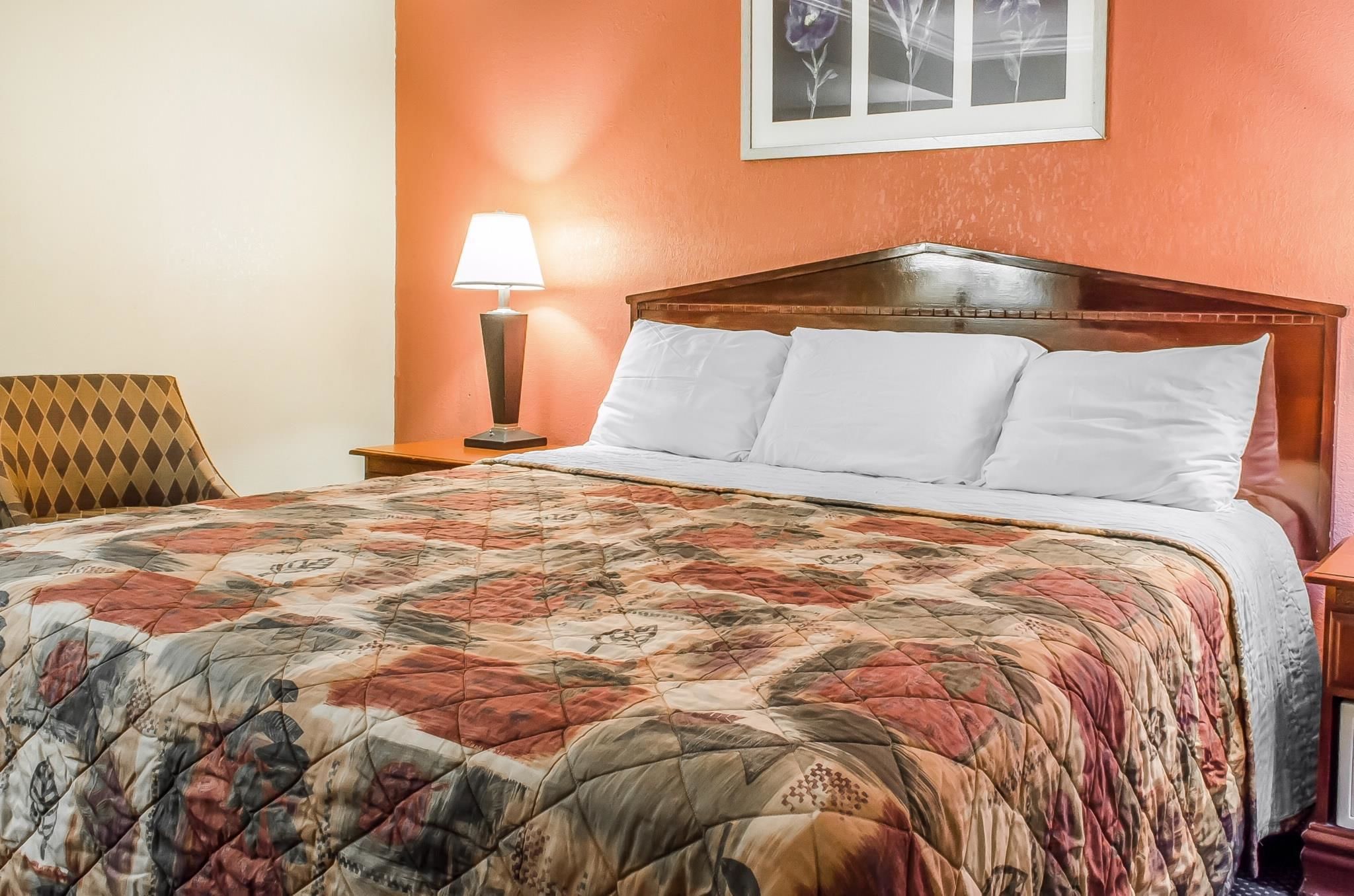 A neatly made bed with a floral quilt, a wooden headboard, and a nightstand with a lamp.