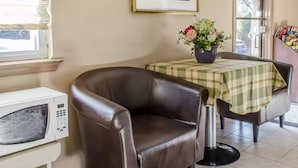 A room with a brown leather chair, a table with a checkered tablecloth, a white microwave, and a framed picture on the wall. - Rodeway Inn Allentown South (Allentown)