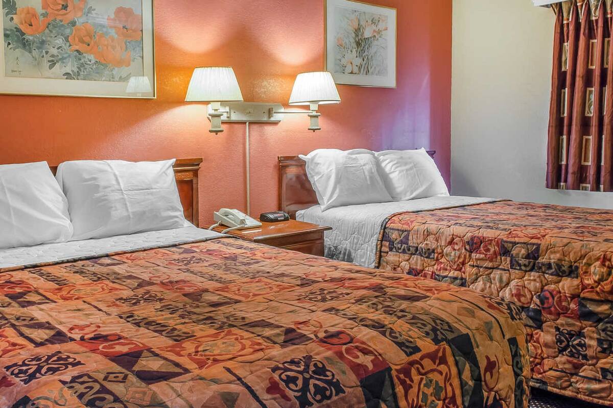 A hotel room with two beds, a nightstand with a telephone, and wall-mounted lamps.