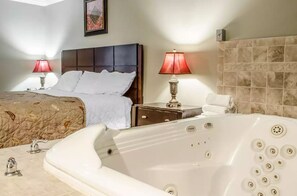 A hotel room with a large white bathtub, a double bed with a brown headboard, two bedside lamps, and a tiled wall. - Rodeway Inn Allentown South (Allentown)