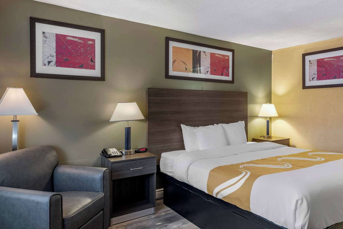 A hotel room with a bed, two bedside tables with lamps, a chair, and artwork on the walls.