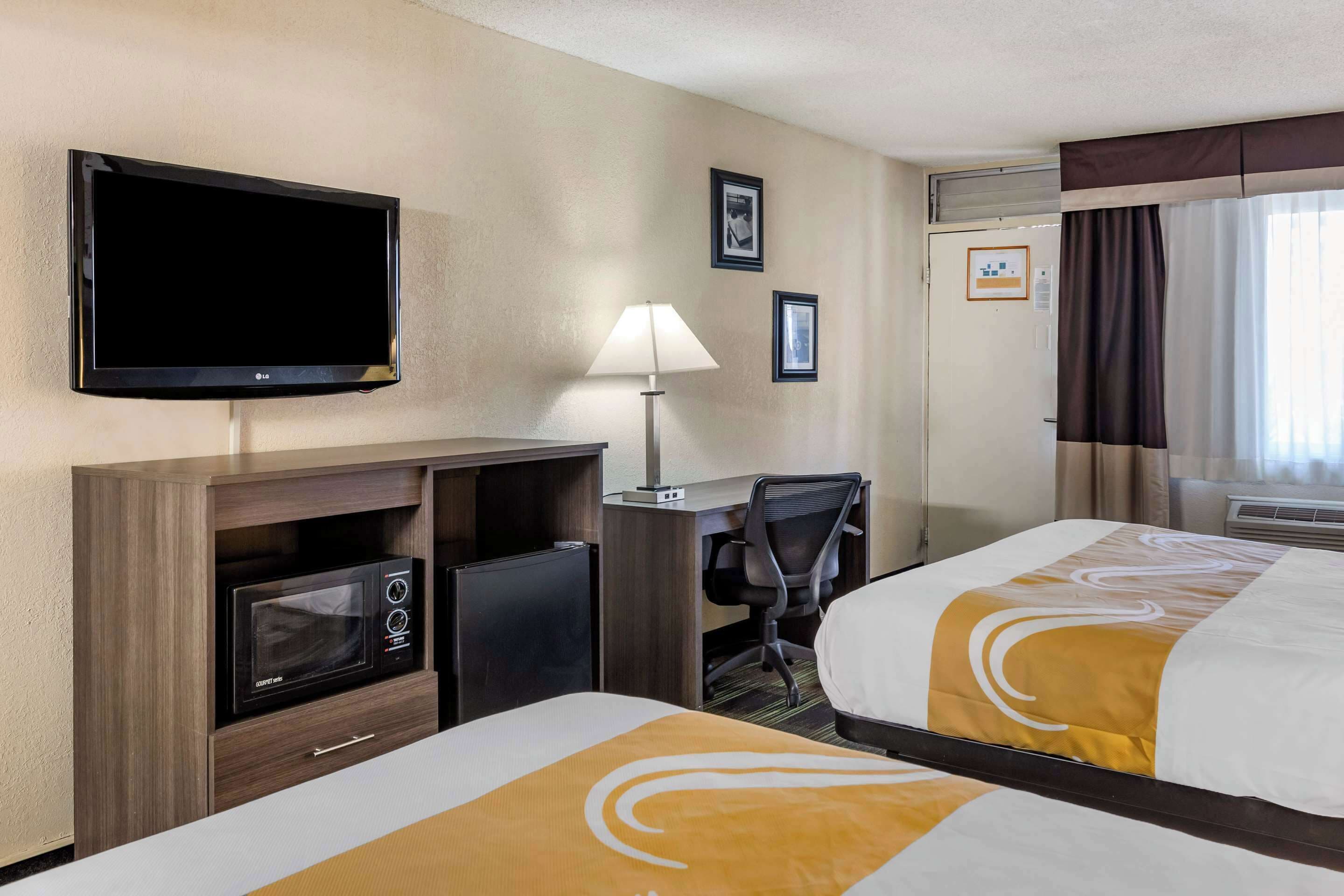 A hotel room with a TV, desk, chair, microwave, and two beds.