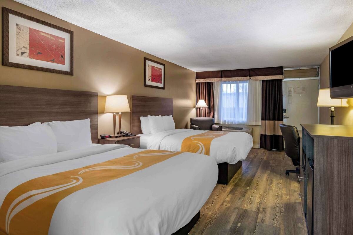 A hotel room with two beds, a desk, a chair, a TV, and a window with curtains.