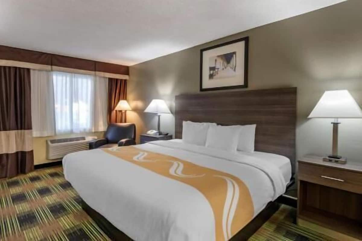 A hotel room with a large bed, two bedside lamps, a chair, a desk, and a framed picture on the wall.