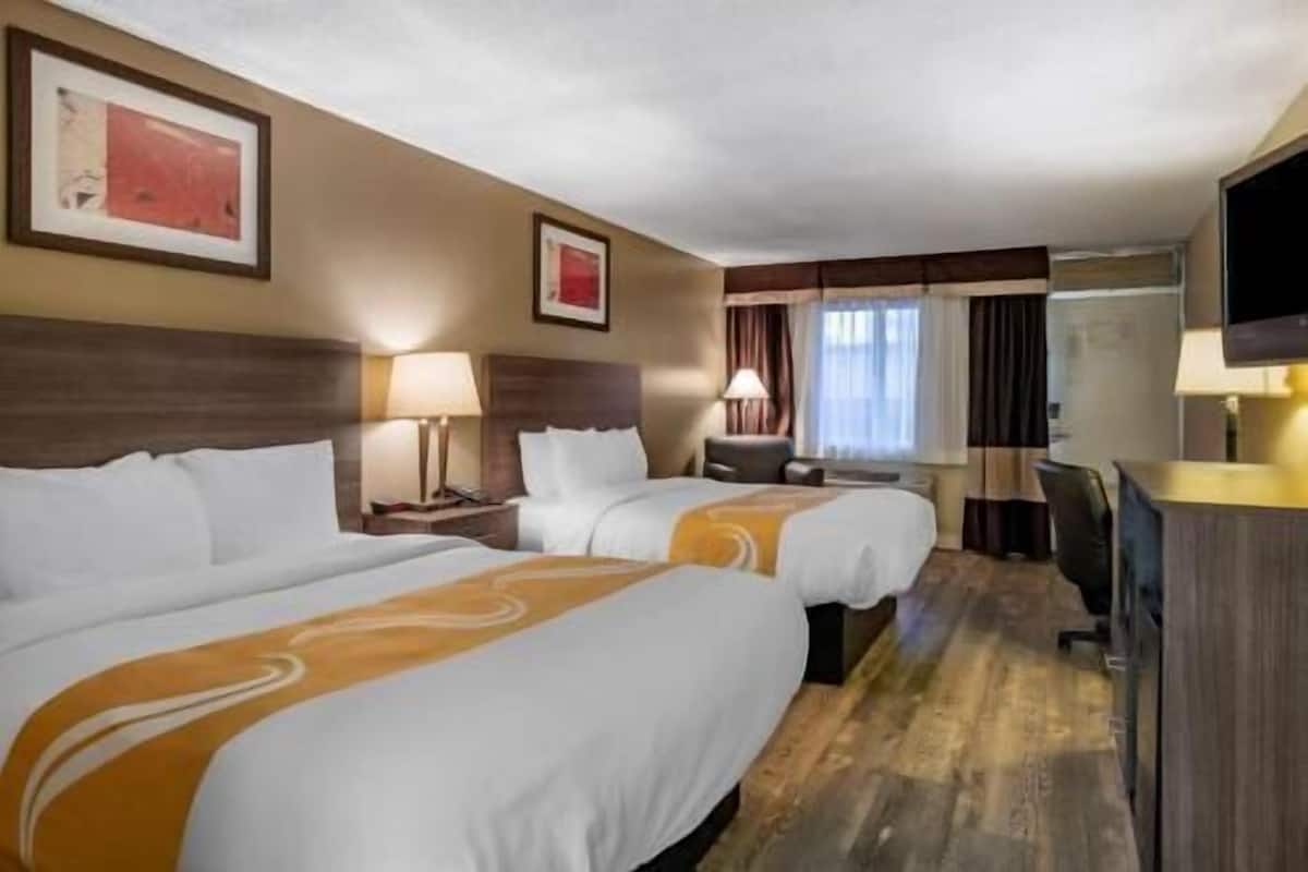 A hotel room with two beds, a desk, a TV, and a window with curtains.
