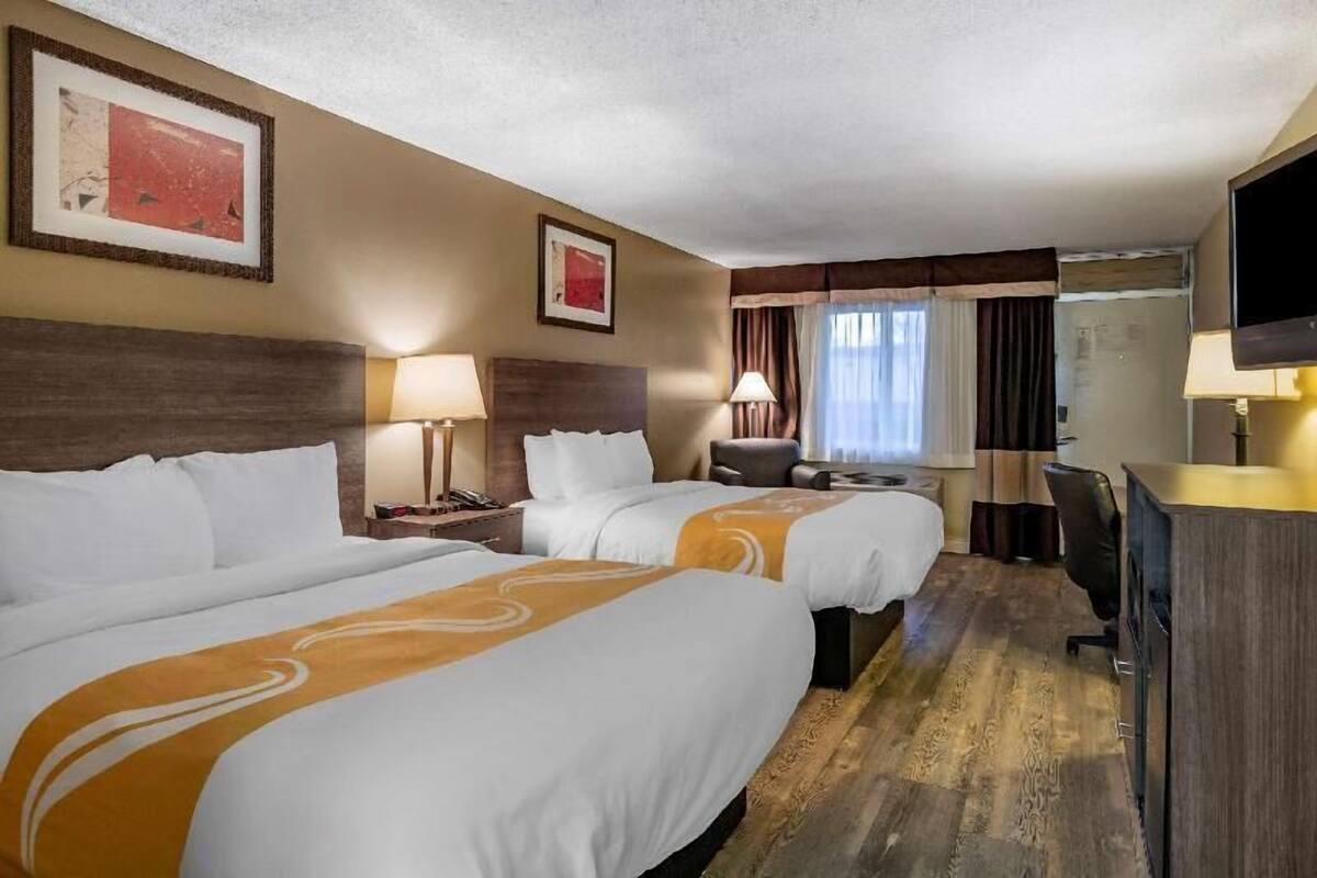 A hotel room with two beds, a desk, a chair, a TV, and artwork on the walls.