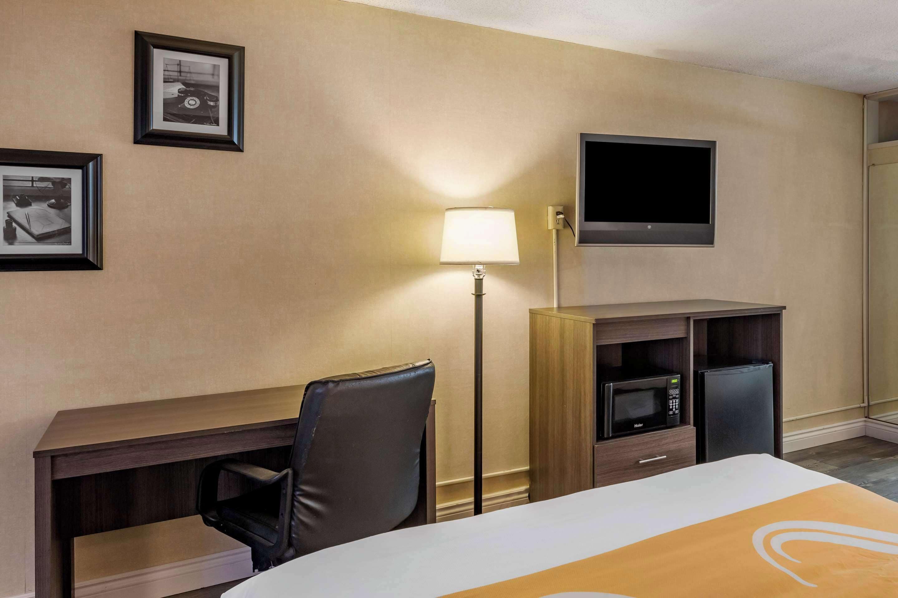 A hotel room with a bed, a desk, a chair, a TV, a lamp, a microwave, and a refrigerator.