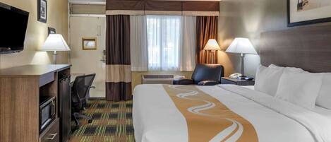 A hotel room with a bed, desk, chair, television, and a window with curtains.