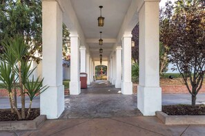 A covered walkway with white columns and hanging lanterns, leading to a fountain. - Quality Inn Barstow Route 66 (Barstow)