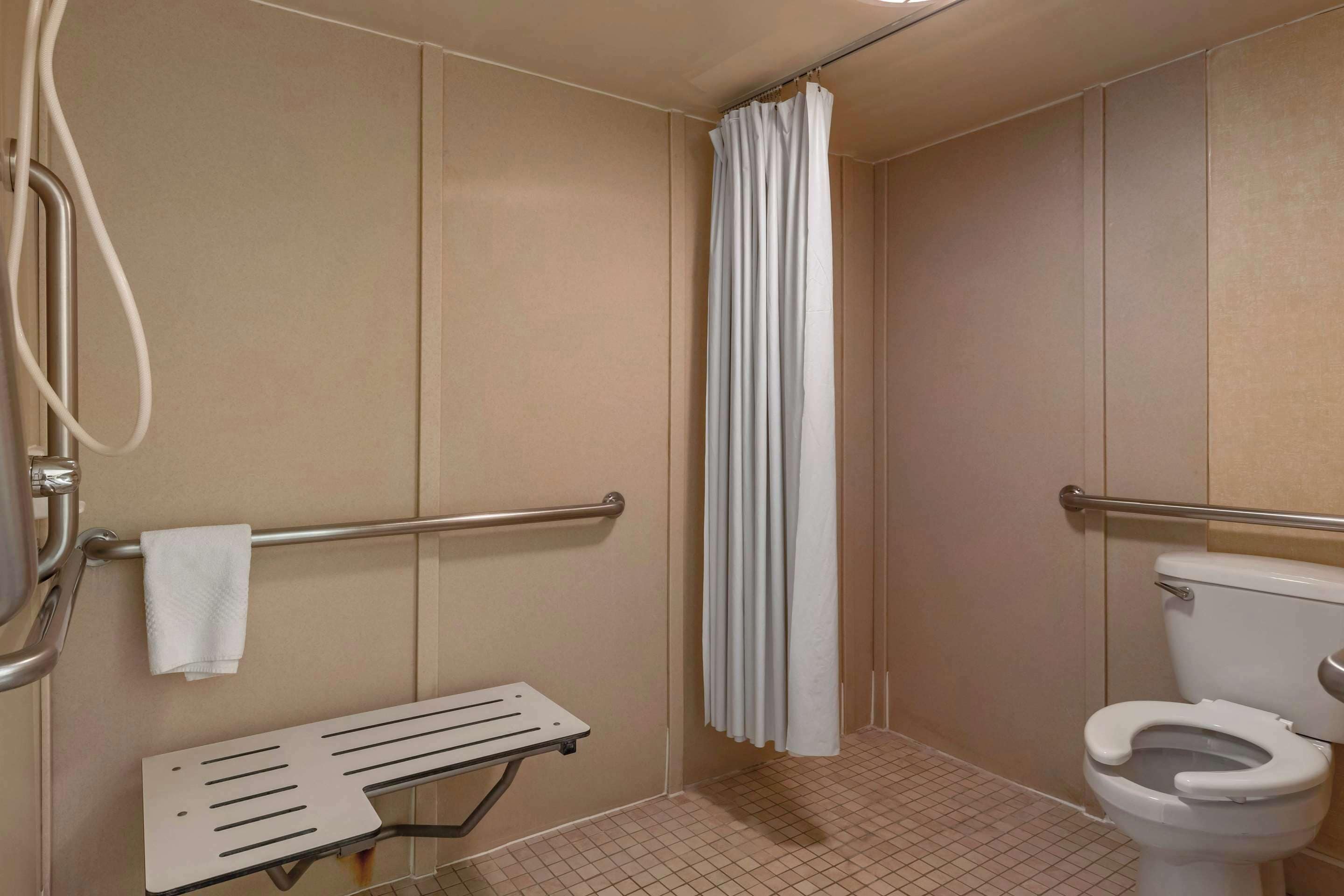 A bathroom with a toilet, a shower with a curtain, a grab bar, and a towel rack.