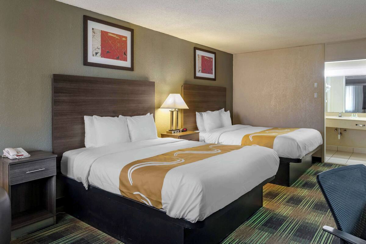 A hotel room with two beds, a nightstand with a phone, a lamp, and a mirror.