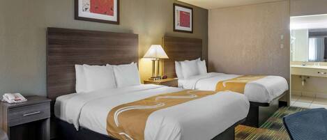 A hotel room with two beds, a nightstand with a phone, a lamp, and a mirror.