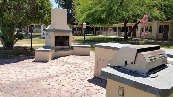 An outdoor patio area with a stone-tiled floor, a built-in grill, and a fireplace.