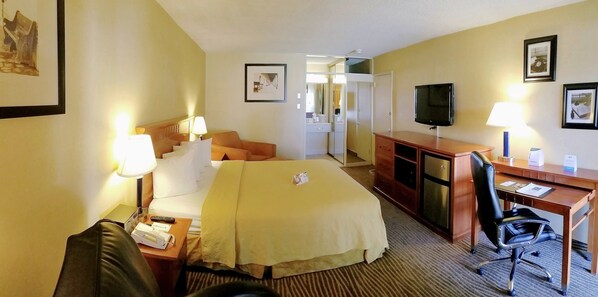 A hotel room with a bed, desk, chair, TV, and a bathroom visible through an open door.