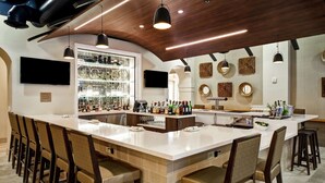 A bar area with a long counter, multiple stools, and a variety of bottles and glasses. - Embassy Suites by Hilton Milpitas Silicon Valley (Milpitas)