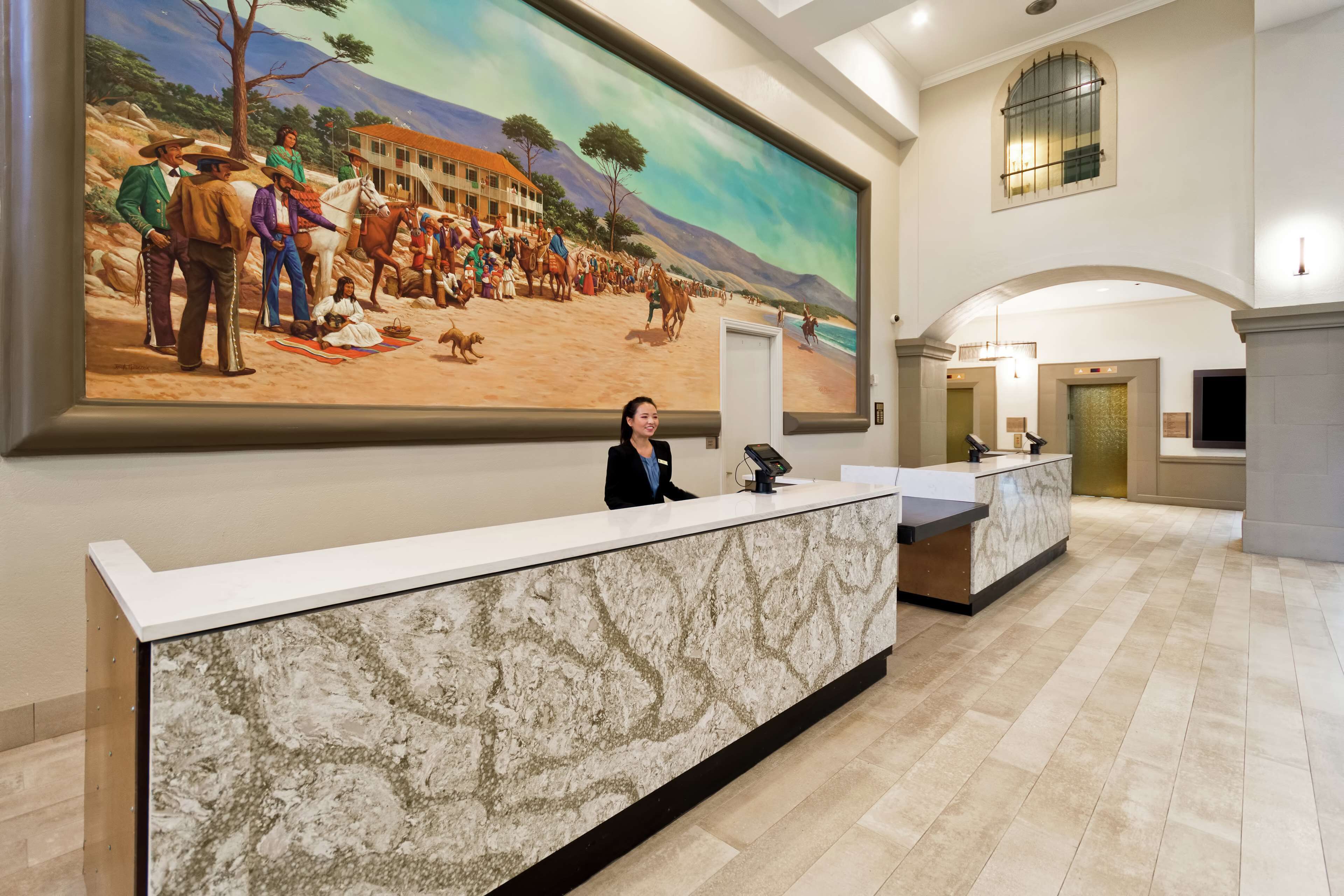 A hotel reception area with a marble counter, a large historical painting on the wall, and a modern interior design.