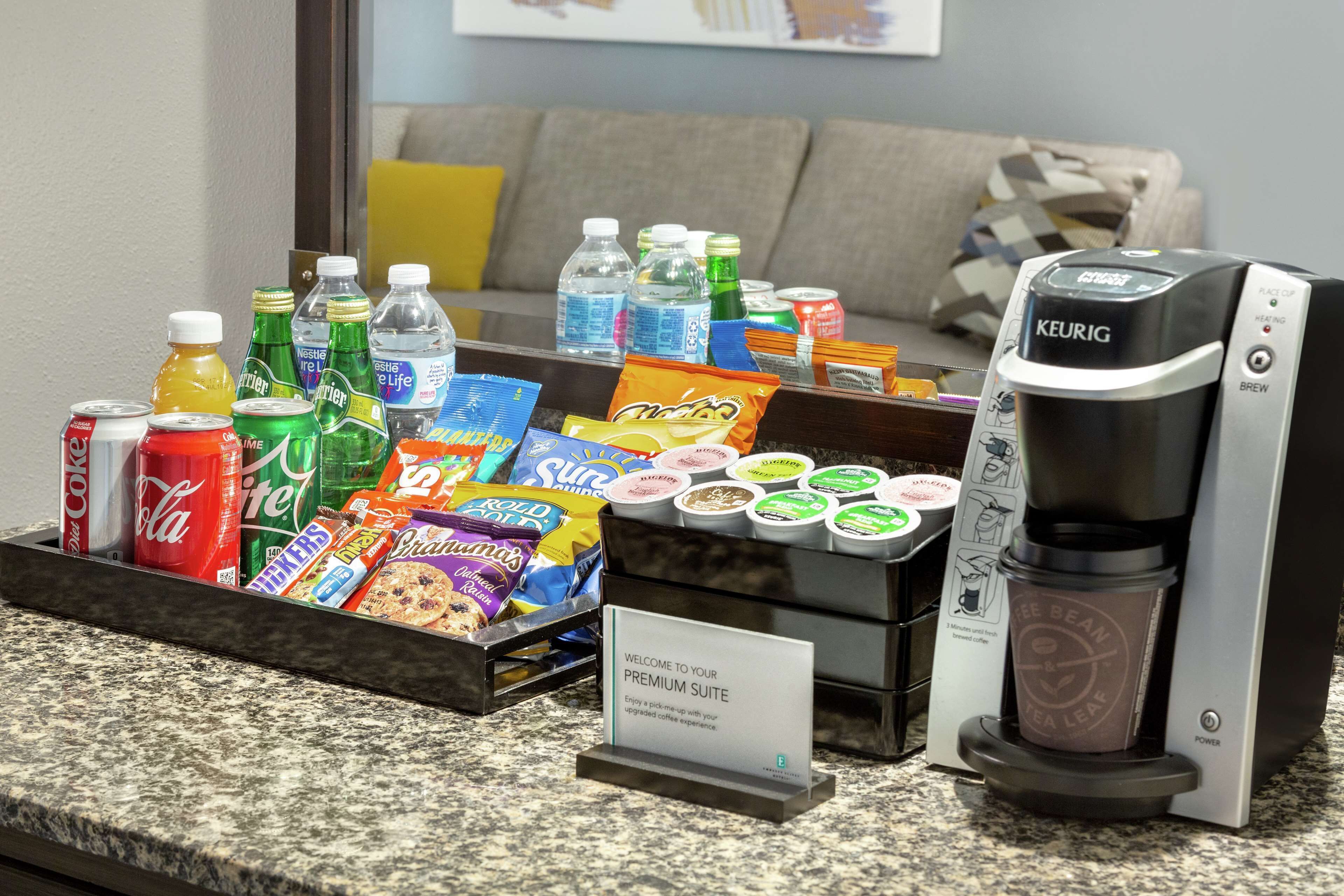 A coffee station with a Keurig machine, various beverages, snacks, and a sign welcoming guests to the premium suite.