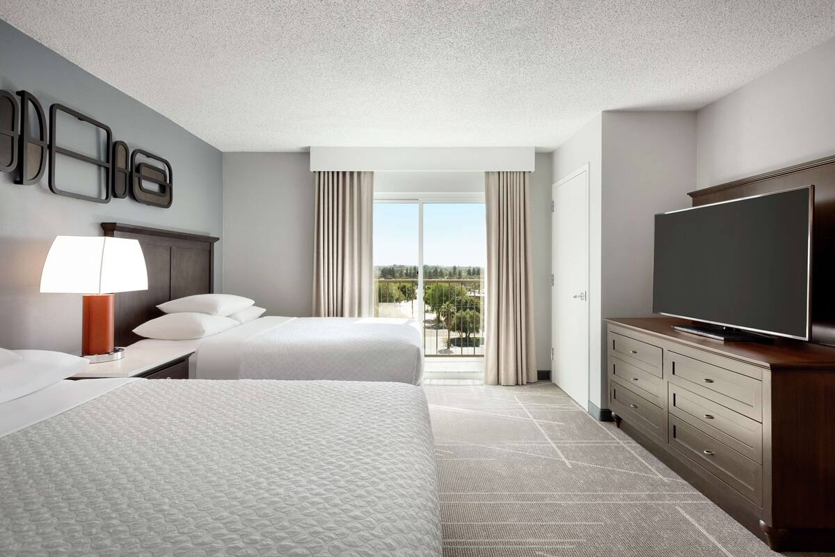A hotel room with two beds, a television, a dresser, and a view of the outdoors.