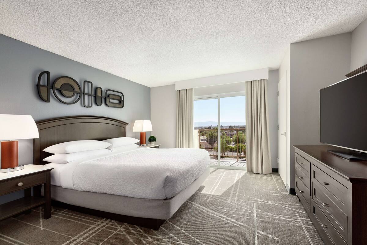 A modern hotel room with a large bed, a flat-screen TV, and a city view.