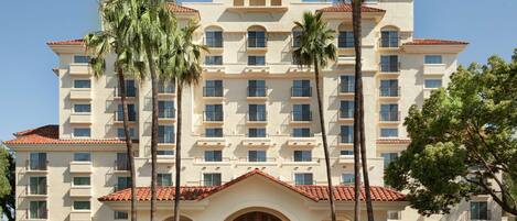 A multi-story hotel with a central entrance, palm trees, and a dome-shaped roof.