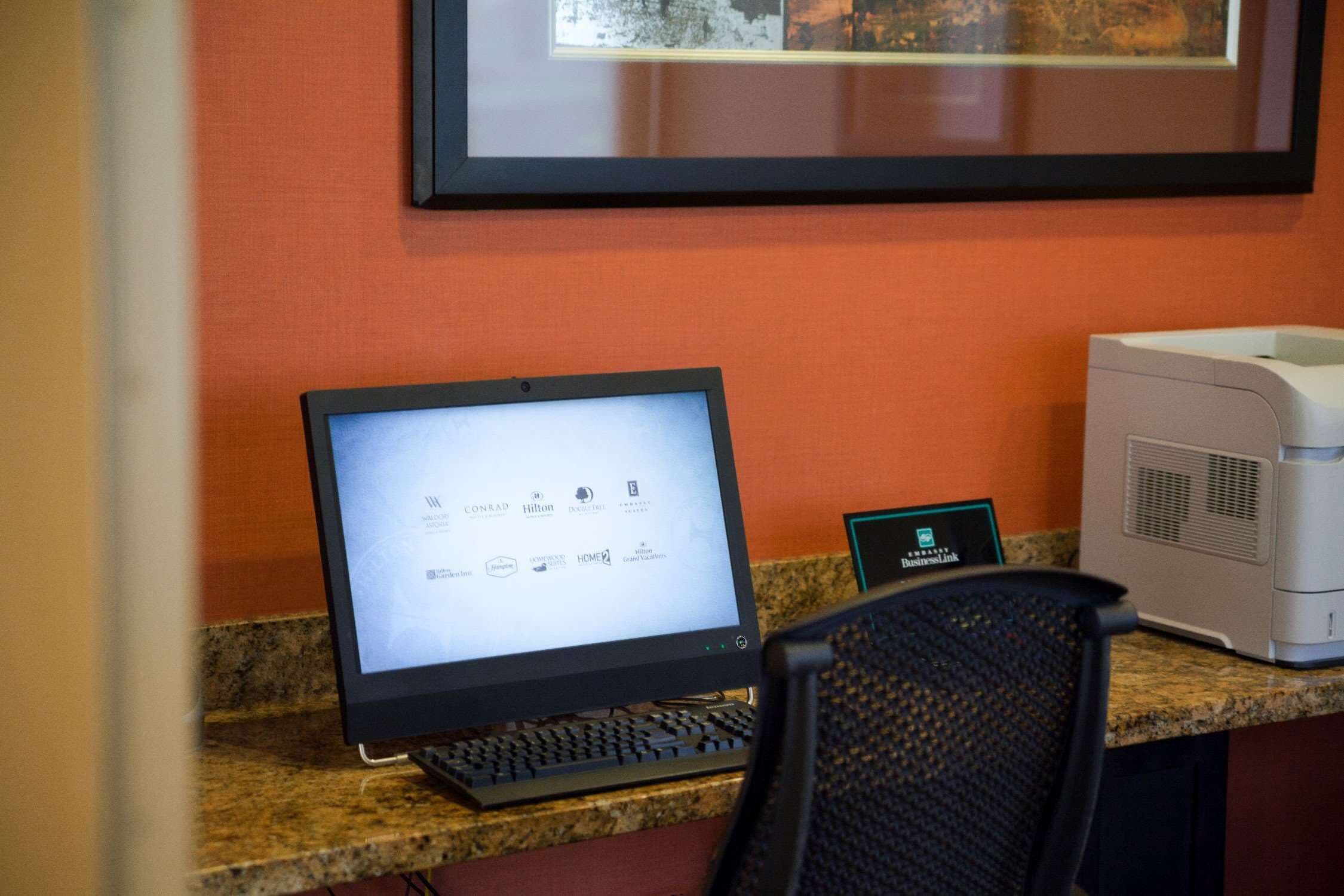 A hotel reception desk with a desktop computer, a printer, and a framed picture on the wall.