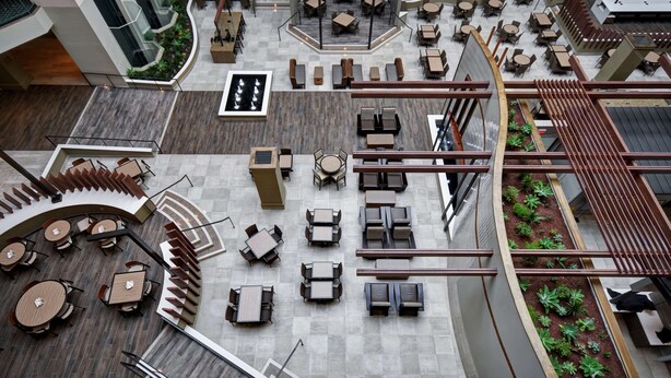 A spacious indoor courtyard with multiple seating areas, including round tables and sofas, surrounded by wooden railings and planters. - Embassy Suites by Hilton Milpitas Silicon Valley (Milpitas)