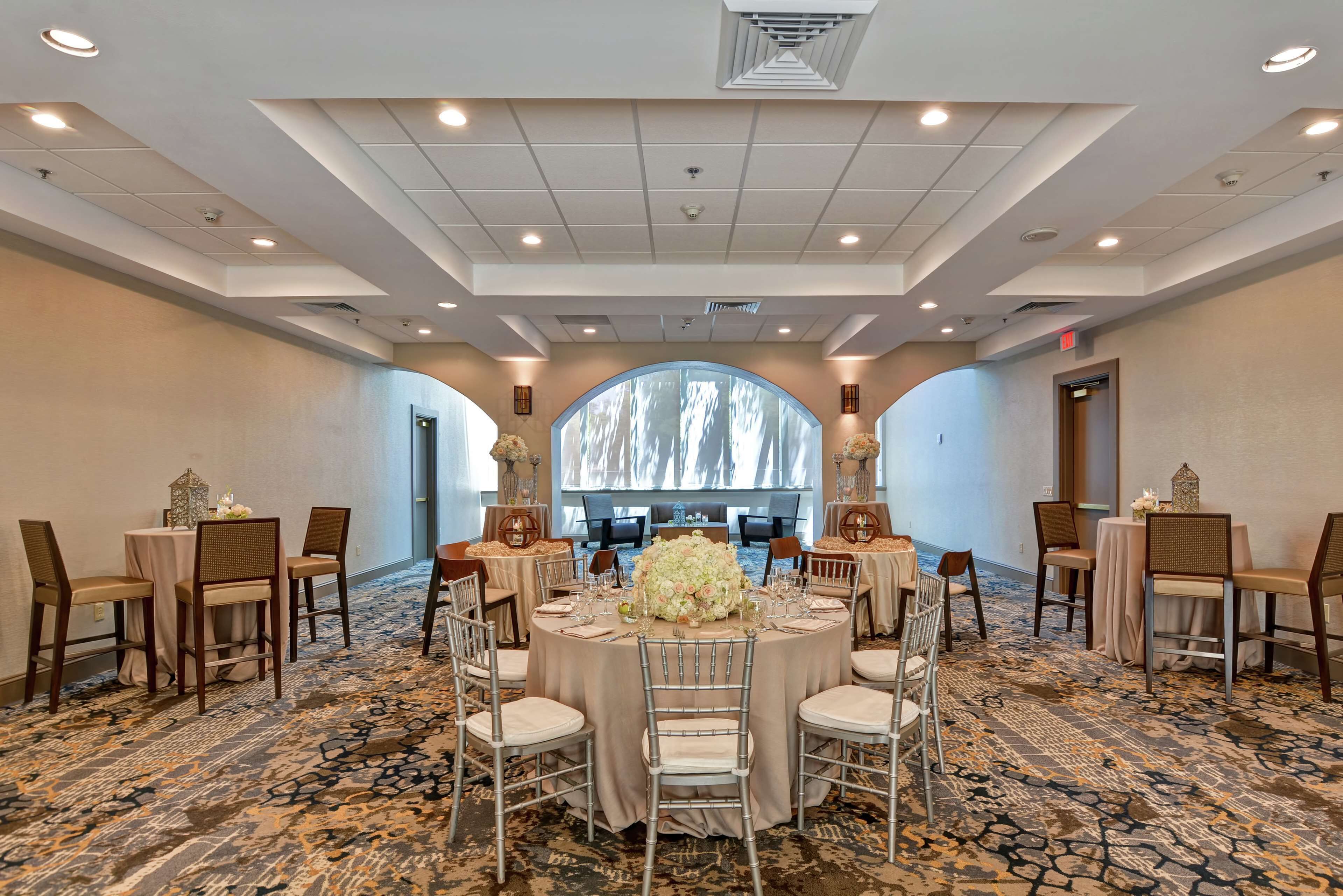 A banquet hall with round tables, chairs, and a large floral centerpiece.