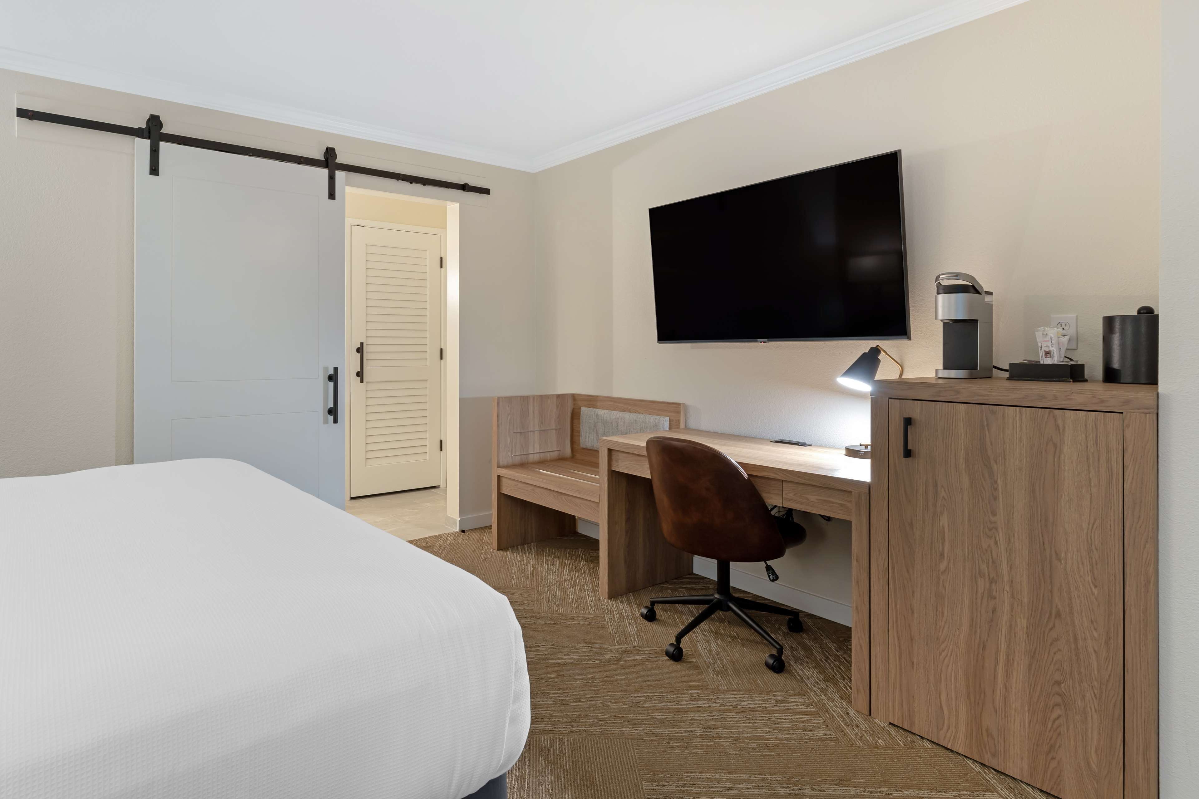 Ein Hotelzimmer mit Bett, Schreibtisch, Computer, Fernseher und Kaffeemaschine.