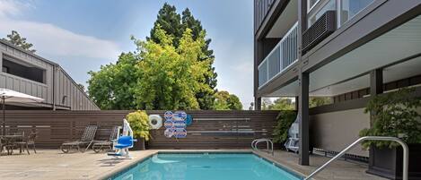 A swimming pool with lounge chairs and a signboard, surrounded by a wooden fence and trees.