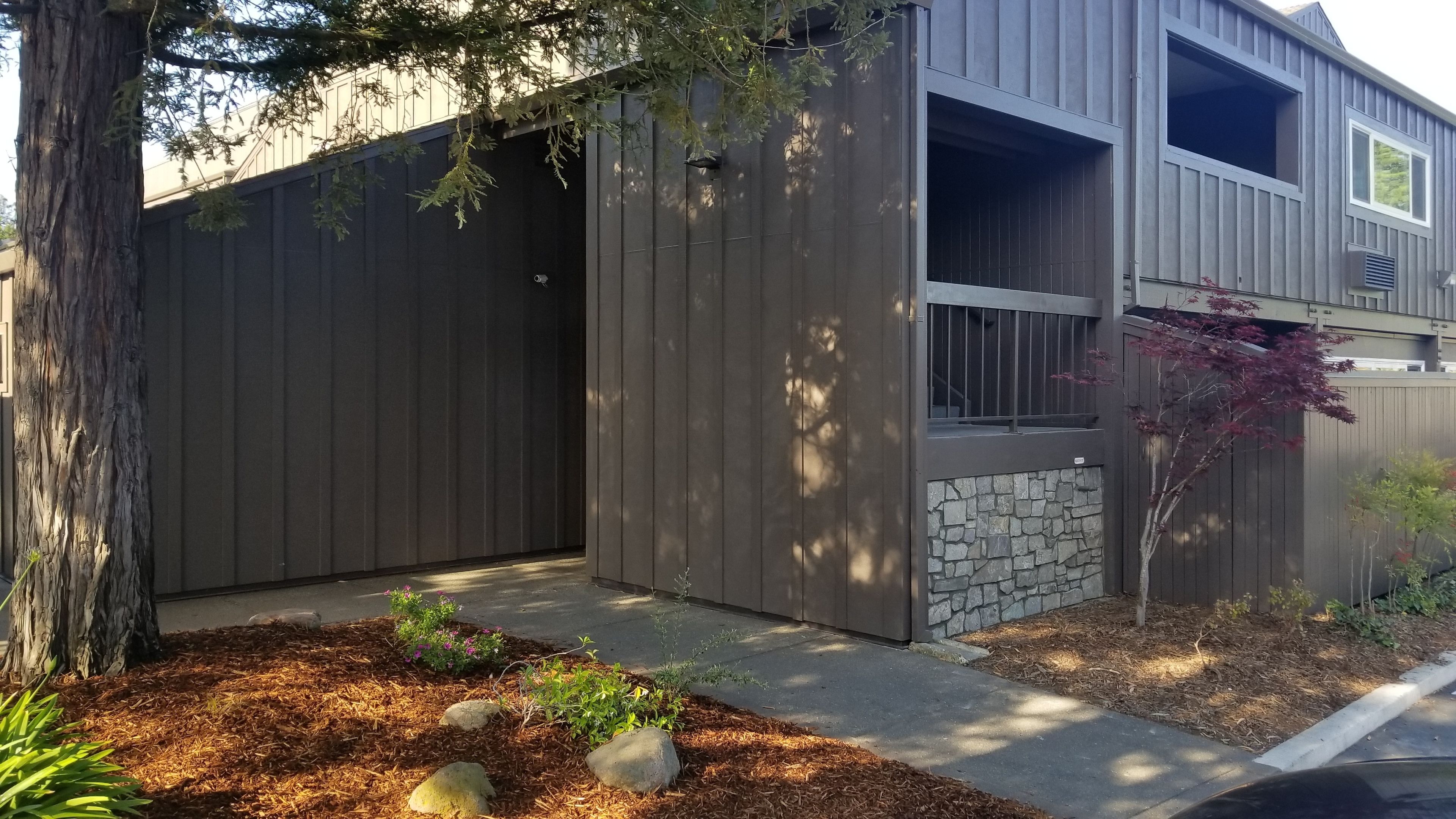 A modern two-story house with a grey exterior, a stone accent wall, and a well-maintained garden with mulch and rocks.