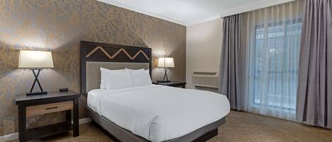 Une chambre d’hôtel avec un grand lit, deux tables de chevet avec des lampes, une tête de lit ornée d’un motif en zigzag, un mur avec un motif doré et une fenêtre avec des rideaux.
